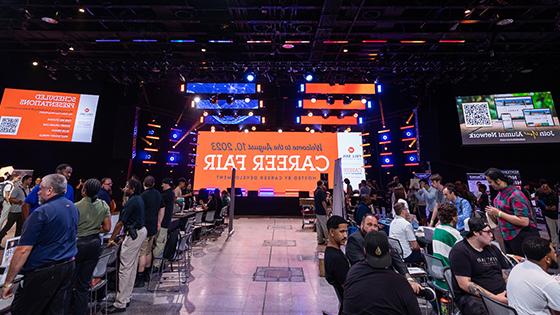 一个热闹的招聘会，有几个摊位. In the center, a giant LED screen welcomes guests to the Career Fair.